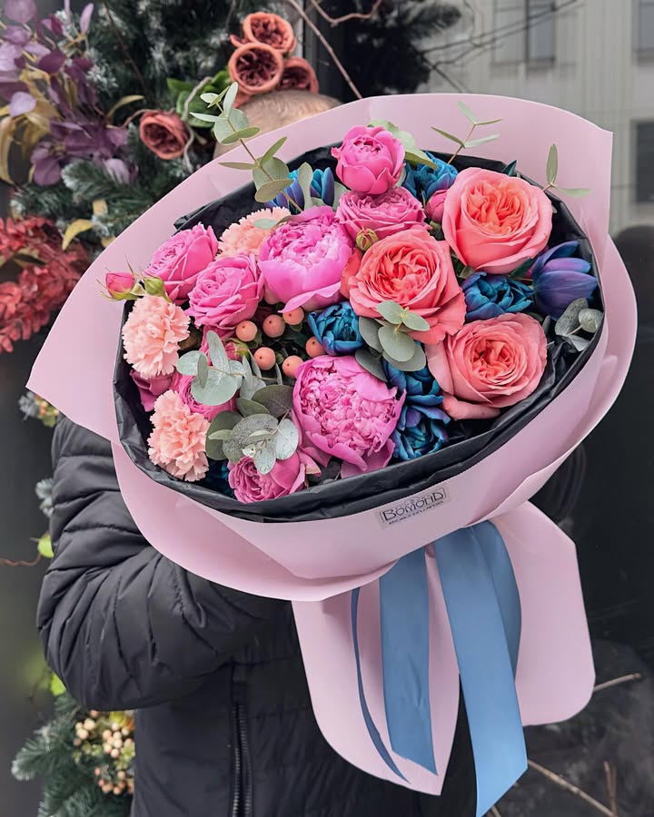 Large bouquet with peonies, roses and blue flowers in stylish pink wrapping