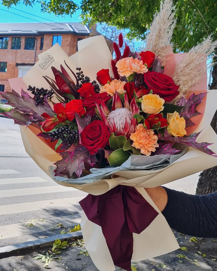 Autumn bouquet with red and yellow roses and protea