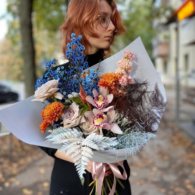 Яскравий букет з блакитними дельфініумами, помаранчевими хризантемами та ніжною орхідеєю